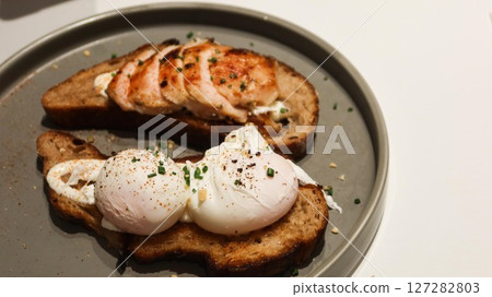 close up of poached egg on a sourdough toast and chicken breast on another slice on a grey plate with copy space 127282803