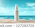 White pump bottle of sunscreen or skincare product standing on beach sand with a bright blue ocean and sky in the background. Ideal summer-themed product mockup for sun protection or beach beauty camp 127283720