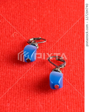 Close-up of a earrings with blue cat's eye effect. Red background. Zircon inserts 127284740