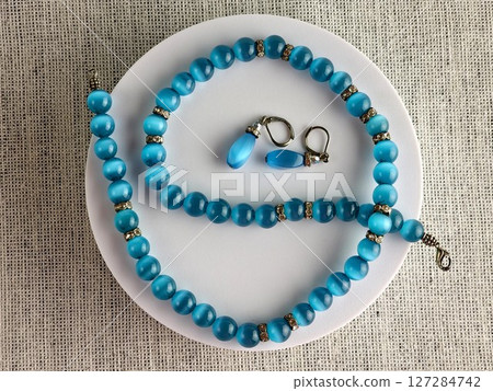 Set of a necklace and earrings with blue cat's eye effect. White background. Zircon inserts 127284742