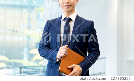 Smiling male businessman holding a binder Smiling male businessman holding a binder 127285235