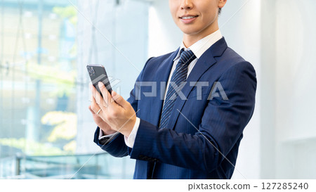 Smiling male businessman holding a smartphone 127285240