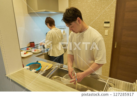 A couple doing housework together in the kitchen A couple doing housework together in the kitchen 127285917