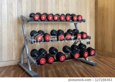 Stand with various dumbbells, weight training equipment, black dumbbell set on rack in modern sport fitness center. Stand with various dumbbells, weight training equipment, black dumbbell set on rack in modern sport fitness center. 127286361