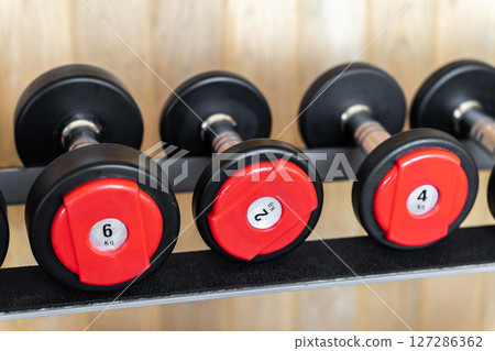 Stand with various dumbbells, weight training equipment, black dumbbell set on rack in modern sport fitness center. Stand with various dumbbells, weight training equipment, black dumbbell set on rack in modern sport fitness center. 127286362
