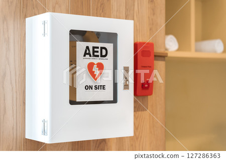 General view of a life saving defibrillator. Portable automated external defibrillator (AED) mounted on the wall in public restroom at airport. 127286363