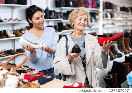 Friendly female sales consultant demonstrates ballet flats to a mature woman customer 127287037