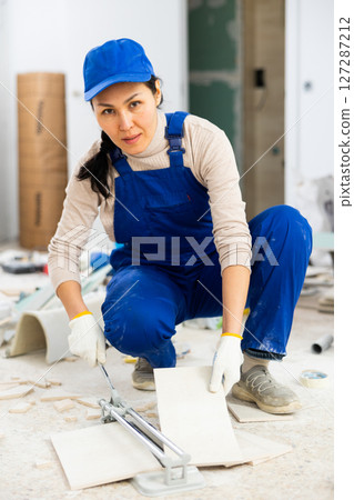 Woman builder cuts ceramic tiles with tile cutter Woman builder cuts ceramic tiles with tile cutter 127287212