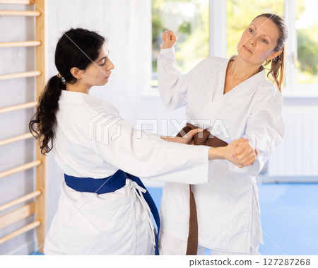 Two woman in kimono sparring together in gym during karate training Two woman in kimono sparring together in gym during karate training 127287268