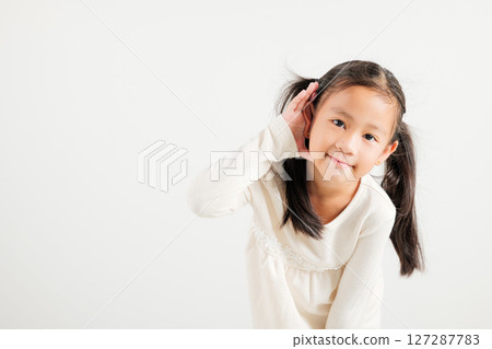 Portrait Asian young child smiling overhearing listening sound to gossip with attention with hand on ear studio shot isolated on white background with copy space hearing gesture, kindergarten kid girl Portrait Asian young child smiling overhearing listening sound to gossip with attention with hand on ear studio shot isolated on white background with copy space hearing gesture, kindergarten kid girl 127287783
