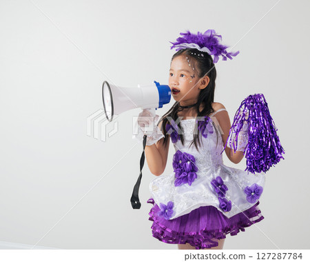Young girl in a purple and white cheerleader costume poses with a megaphone. Studio image on white, capturing her enthusiasm and festive vibe. 127287784