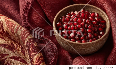 Red Pomegranate Seeds in Rustic Bowl on Maroon Fabric 127288276