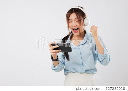 Game joy for woman using phone horizontal as she raises hand to celebrating after game play, full of excitement and mobile fun. watch video online isolated studio white background 127289018