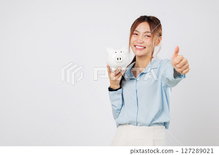 Portrait Happy young Asian woman with piggy bank, giving thumb up, saving piggy money with excitement, showing investment success and personal finance confidence. isolated studio white background 127289021