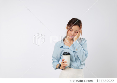 Sleep deprived tired woman covers face with palm, holding coffee paper cup, feeling sad and sleepy, stress from lack of sleep shows in her eyes as she struggles to wake up. isolated white background Sleep deprived tired woman covers face with palm, holding coffee paper cup, feeling sad and sleepy, stress from lack of sleep shows in her eyes as she struggles to wake up. isolated white background 127289022