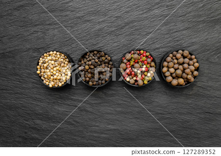 Black, Green, Pink, White and Fragrant Pepper Grains in Round Jars Placed on Black Stone Surface Background 127289352