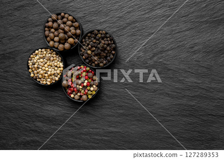 Black, Green, Pink, White and Fragrant Pepper Grains in Round Jars Placed on Black Stone Surface Background 127289353