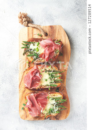 open sandwiches with asparagus and prosciutto, with cheese, breakfast, on a wooden serving board, open sandwiches with asparagus and prosciutto, with cheese, breakfast, on a wooden serving board, 127289514