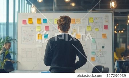 Man in Black Sweater Looking at Whiteboard with Sticky Notes 127290089