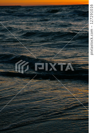 Ocean with waves, sunset sky is orange. water is choppy and waves are crashing on shore. 127291016