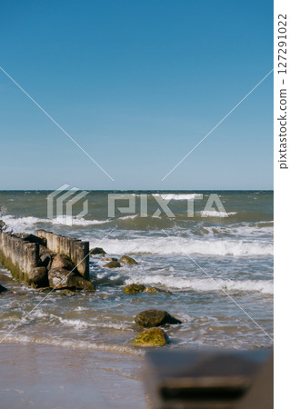 rocky beach with a wooden pier and a pond. The sky is clear and blue.  127291022