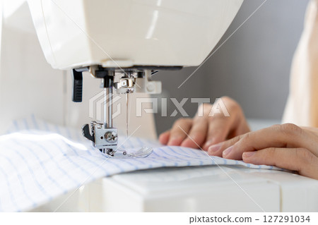 woman sews a light fabric on a sewing machine. making clothes, hobbies. woman sews a light fabric on a sewing machine. making clothes, hobbies. 127291034
