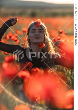 Poppy field woman: Blonde poses with red poppies at sunset for a portrait in the countryside. Poppy field woman: Blonde poses with red poppies at sunset for a portrait in the countryside. 127291095