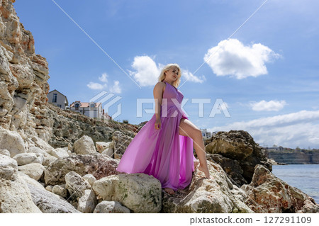 Dress Woman Rocks: Blonde model poses on Malta's rocky coast in the daytime for fashion shoot, smiling. 127291109