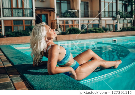 Happy woman in bikini sitting near swimming pool, summer vacation. Happy woman in bikini sitting near swimming pool, summer vacation. 127291115