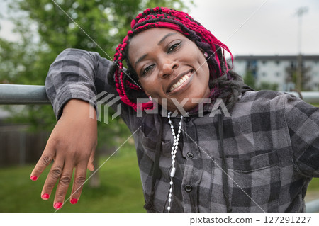 Happy African American Woman with Pink Braids Relaxing Outdoors in Checkered Hoodie 127291227