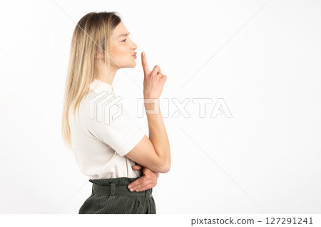 Woman standing profile the camera and showing silence gesture with finger 127291241
