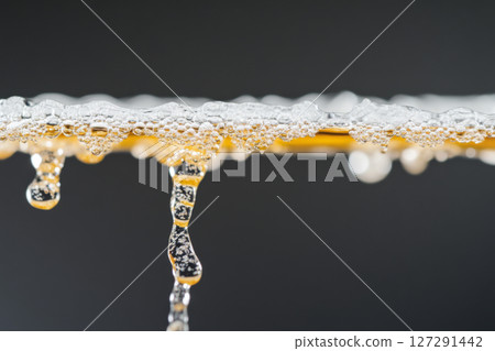 Close-up of water and amber-colored liquid flowing with bubbles, background 127291442
