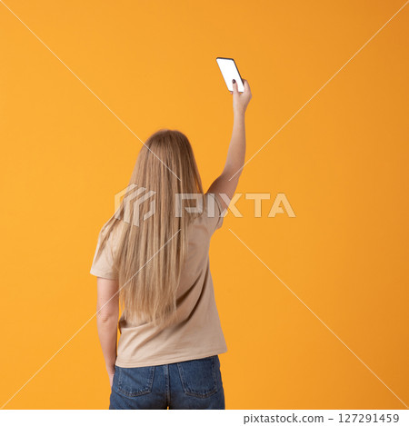 Woman Holding Smartphone Against Orange Background Woman Holding Smartphone Against Orange Background 127291459