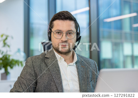 A man in a gray suit and headset looks directly at the camera, possibly working in a customer service or call center. 127291822