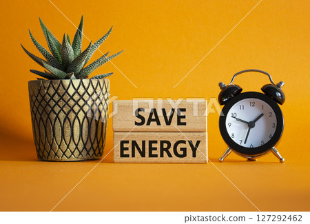 Save Energy symbol. Wooden blocks with words Save Energy. Beautiful orange background with alarm clock and succulent plant. Business and Save Energy concept. Copy space. 127292462