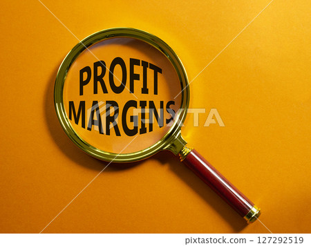 Profit Margins symbol. Magnifying glass with words Profit Margins. Beautiful orange background. Business and Profit Margins concept. Copy space. 127292519