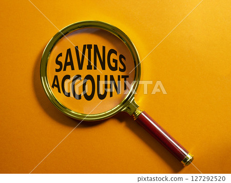 Savings Account symbol. Magnifying Glass with Concept word Savings Account. Beautiful orange background. Business and Savings Account concept. Copy space 127292520