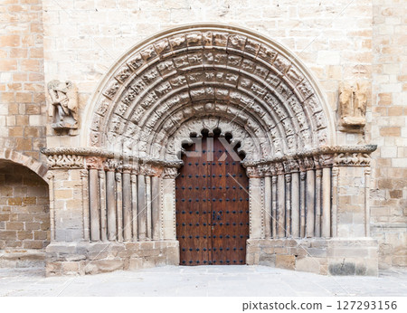 Detailed stone archway and wooden doors of a historic church in Obanos, Spain 127293156