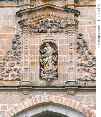 Carved stone sculpture of a figure surrounded by decorative elements on a historical building 127293179