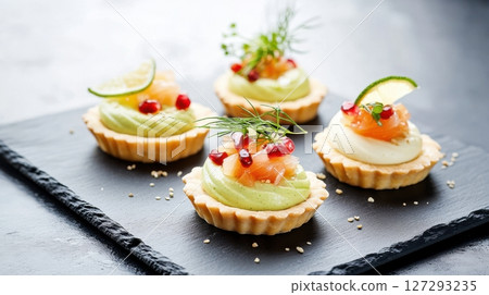 Modern gourmet appetizer with delicate tartlets: silky avocado mousse, vibrant salmon with pomegranate, and bold kimchi tofu, elegantly plated on slate with soft lighting for a high-end presentation. 127293235