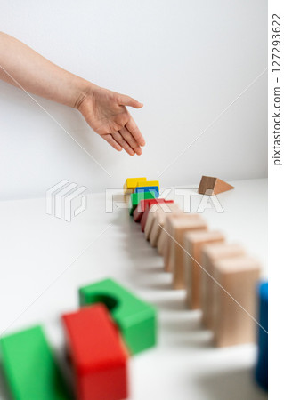 Child hand toppling colorful wooden blocks in domino effect 127293622