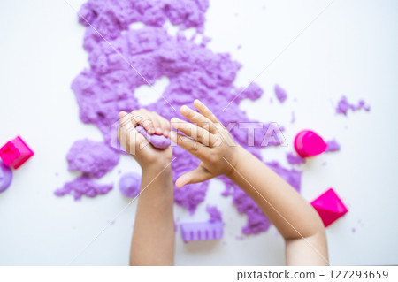 Child hands playing with purple kinetic sand and molds on white background Child hands playing with purple kinetic sand and molds on white background 127293659
