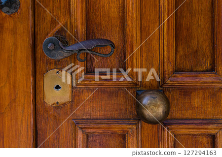Old wooden door of Athens Greece features antique door handle, brass door knob, and keyhole, reflecting the historical architecture and traditional craftsmanship found in the city. Old wooden door of Athens Greece features antique door handle, brass door knob, and keyhole, reflecting the historical architecture and traditional craftsmanship found in the city. 127294163