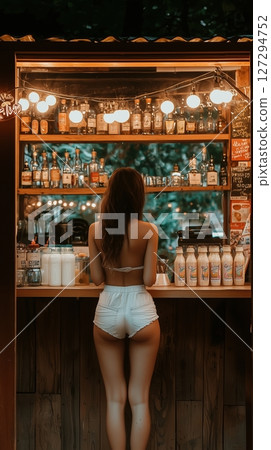 Charming girl enjoying a refreshing drink at an outdoor bar with twinkling lights in the evening 127294752