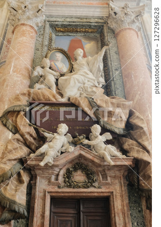 Ornate baroque tomb monuments inside Saint Peters Basilica featuring dynamic marble sculptures of angels religious figures and symbolic drapery carved into grand architectural settings. High quality 127296628