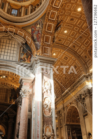 Decorative golden coffered ceiling and detailed pillars with frescoes and carvings inside Saint Peters Basilica showcasing baroque Catholic architecture in Vatican City. High quality photo 127296662