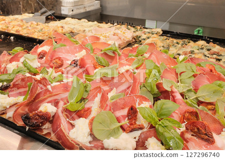 Authentic Italian street food in Rome with takeaway pizza and soft drink on stone pavement and pizza counter full of toppings traditional cuisine. High quality photo 127296740