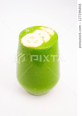 green smoothie with banana slices served in clear glass on white background healthy detox drink with tropical fruit topping. High quality photo 127296808