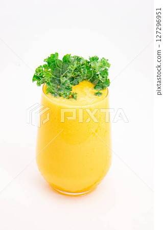 yellow fruit smoothie or juice served in clear glass and garnished with fresh curly kale on clean white background. High quality photo 127296951
