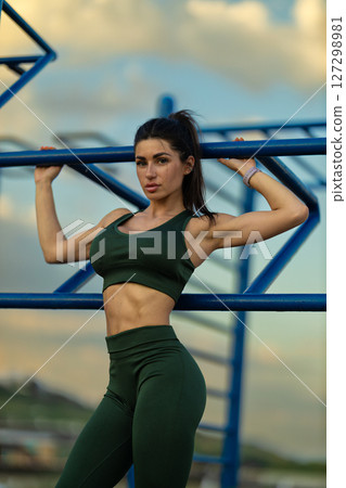 On a vibrant sports ground near the sea, a sporty girl strikes a confident pose, displaying her toned physique in activewear as the clouds drift above On a vibrant sports ground near the sea, a sporty girl strikes a confident pose, displaying her toned physique in activewear as the clouds drift above 127298981